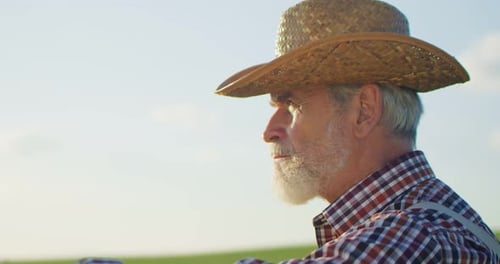 Close Up of the Senior Caucasian Good Looking Wise Man Farmer in a Hat Looking at the Field Turning