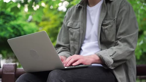 A young male freelancer works at his laptop in the park. Close-up