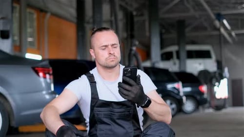 Man on Garage Floor Phone in Hand Surrounded By Automotive Gear and Equipment