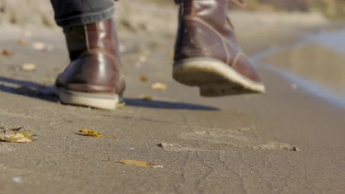 Walking by the ocean on a Sandy beach in Fall. Close-up of men's leather fashion boots. Walk along a