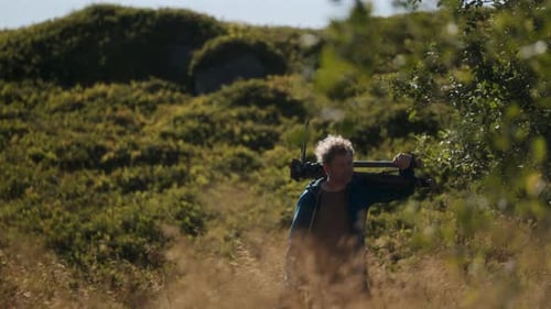 Man walking through field with tripod