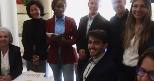 Un equipo empresarial multigeneracional sonríe ante la cámara durante una reunión inclusiva de intercambio de ideas en la oficina de EE. UU.