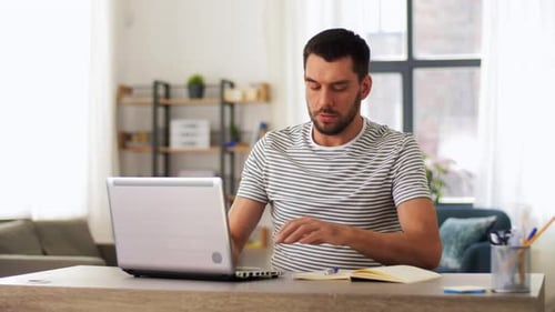 Young hispanic man working remotely from home office with laptop and notebook