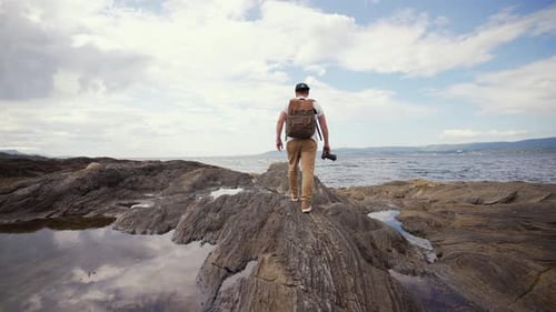 With the Mountains of Norway As a Backdrop a Lone Man with a Backpack Walks Along a Sandy Beach