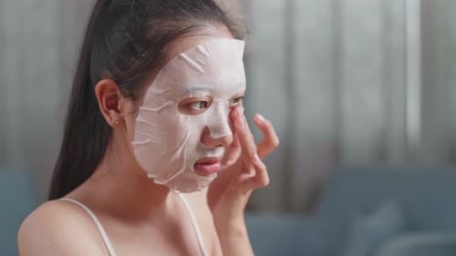 Close Up Of Beautiful Young Asian Woman Applying Sheet Facial Mask And Smiles To Camera