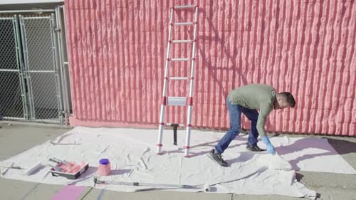 Mature man volunteering spreading drop cloth and painting at sunny orange wall