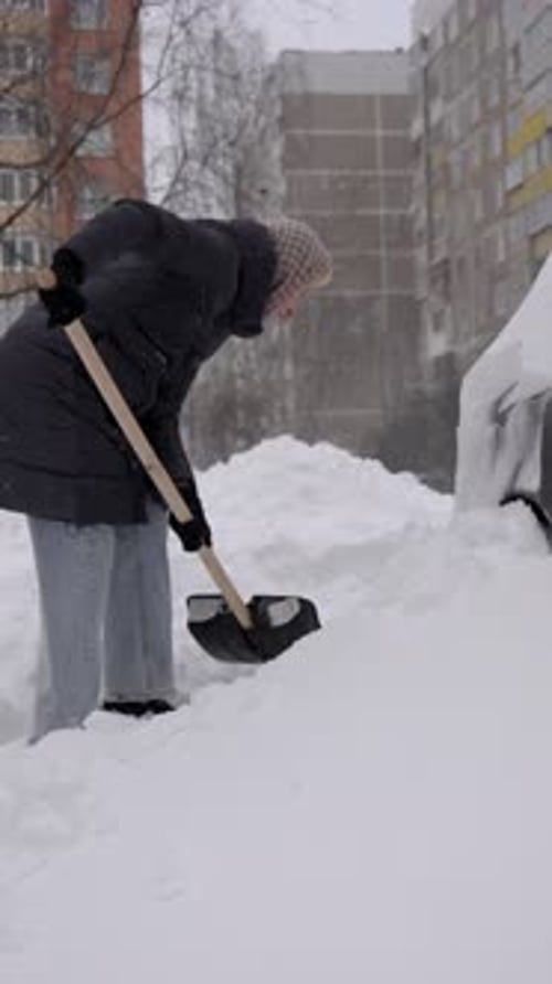 Woman shoveling snow in front of car outdoors