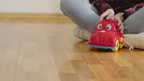 Child Plays with Red Toy Car on Floor