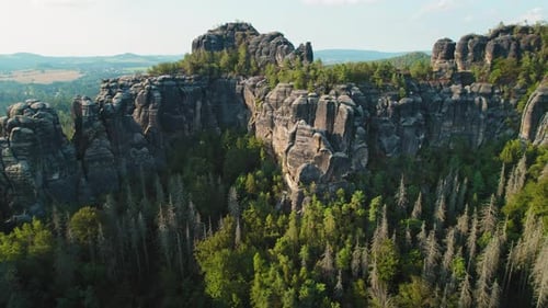 Towering cliffs with jagged edges rise from a dense forest, contrasting the serene surrounding valle