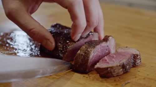 Cutting fried steak into pieces on a wooden cut board with a steel knife. Close up. Homemade cooking