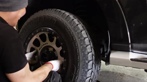 Hand-held shot of a mechanic putting a wheel and bolts back on a car
