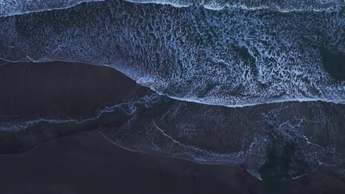 Drone aerial view looking straight down over white waves crashing on a beach