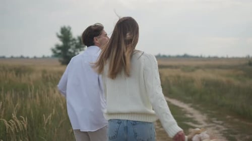 Back View Joyful Young Couple Holding Hands Running in Slow Motion in Autumn Field Pointing Away