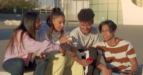 Group of Multicultural Happy Teenage Friends Looking the Phone and Laughing in a Bench in the City