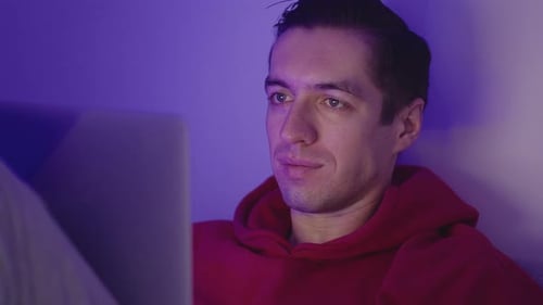 Young Man Using Laptop Computer While Lying in the Bedroom at Home at Nighttime