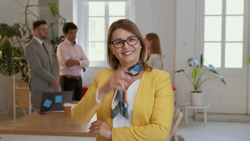 Portrait of smiling businesswoman in office with her colleagues in background.