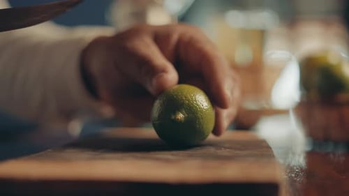 Close up of male hands passing by lime and slicing on half on wooden board with knife, slow motion
