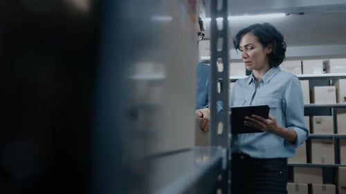 Female Inventory Manager Shows Digital Tablet Information to a Worker Holding Cardboard Box, They T