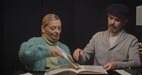 Pareja de ancianos organizando fotos recién desarrolladas en un álbum de fotos vintage