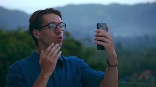 Hombre milenario usa un teléfono inteligente para una videollamada y habla con amigos sobre un fondo natural, jovencito