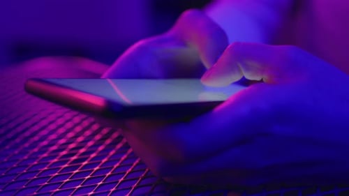 Typing on mobile phone in vibrant neon party lights abstract concept