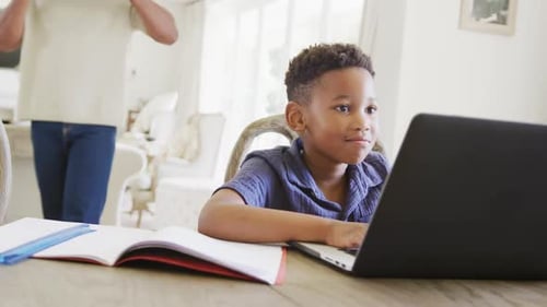 Happy african american boy using laptop for online lesson, in slow motion