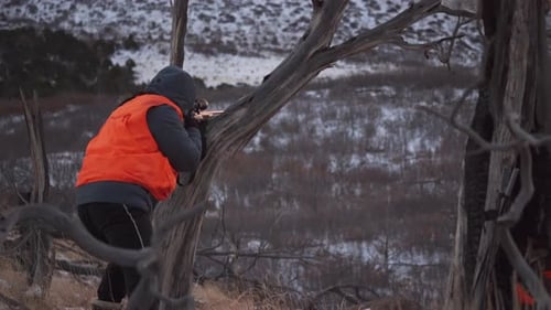 Hunter Aiming Rifle Through Trees In Mountain Landscape