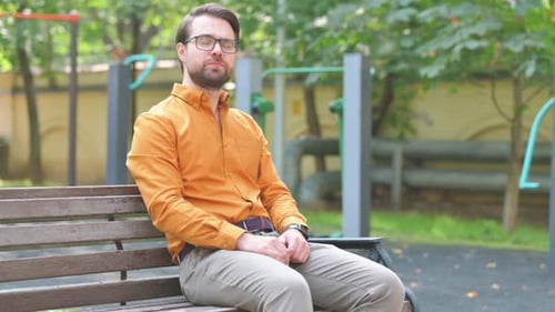Man Sitting on Bench in Urban Park