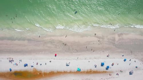 Top-down view of turquoise shoreline with beachgoers and umbrellas