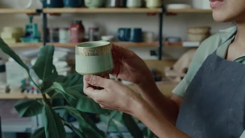 Close-up of Young Woman Holding and Examining Glazed Ceramic Cup in Studio