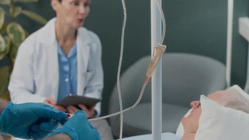 Worker Setting up IV Drip for Senior Patient Talking to Doctor in Hospital Ward