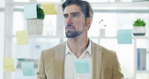 4k video footage of a handsome young businessman writing notes on a glass wall in his office