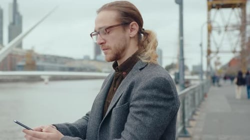 Businessman Texting on Phone and Smiling on City Riverside