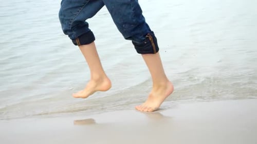 Closeup slow motion of child's feet running on sandy sea beach and splashing water
