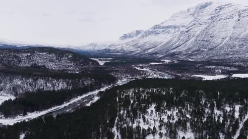 Aerial footage of icy mountains, snow-covered forest, and winding river in Norway