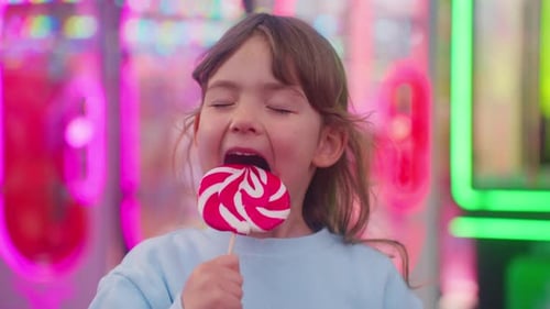 Happy Smiling Little Girl in Amusement Park Child with a Large Candy on a Stick in Her Hand Smiles