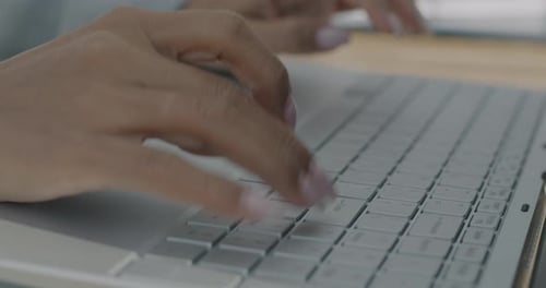 Nahaufnahme weiblicher Hände, die mit der Laptoptastatur tippen, während eine Geschäftsfrau online am Computer arbeitet
