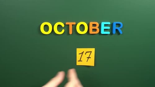 Hand sticking a sticker 17 October calendar day on school board. 17 date of October. Seventeenth