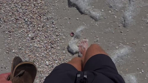 Bare feet walking on seashell-covered sandy beach