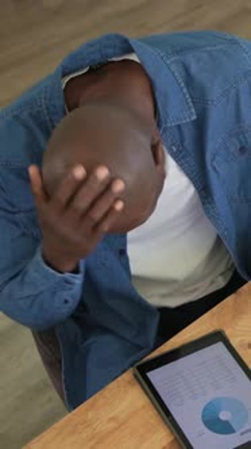 Vertical video: Wiping mouth, senior in denim tapping tablet at dining table, viewing pie chart