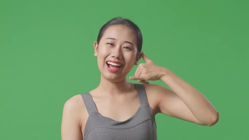 Woman Wearing Sportswear And Showing Call Me Gesture And Smiling To Camera On Green Screen