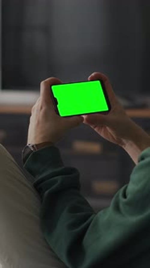 Person Relaxing Indoors and Holding Smartphone with Bright Green Screen Mockup Watching or Browsing
