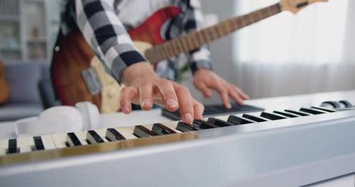 Close up of male hands playing midi piano keyboard and synthesizer in home studio.