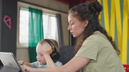 Curious Little Boy with Wireless Headphones is Looking at Display of Tablet Viewing Cartoons