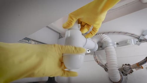 A Plumber in Gloves Collects a Siphon Under the Sink