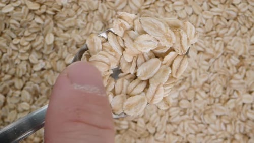 I shake off oat flakes from the spoon with my finger. Close-up against the background of oats.