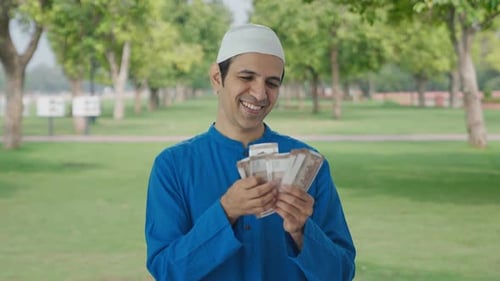 Happy Muslim man counting money in park