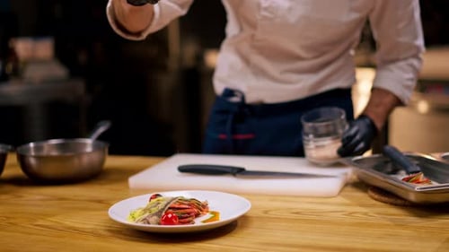 Close Up Chef in a White Tunic Holding a Bowl and Pouring Sauce From Spoon Onto the Finished Dish