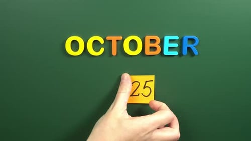 Hand sticking a sticker 25 October calendar day on school board. 25 date of October. Twenty fifth