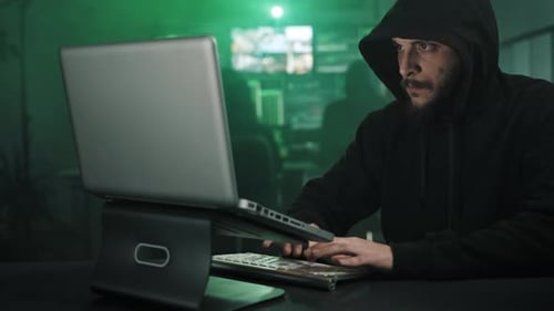 Un hacker cagoulé travaillant dans un sous-sol sombre et caché attaque les serveurs de données du gouvernement et infectant
